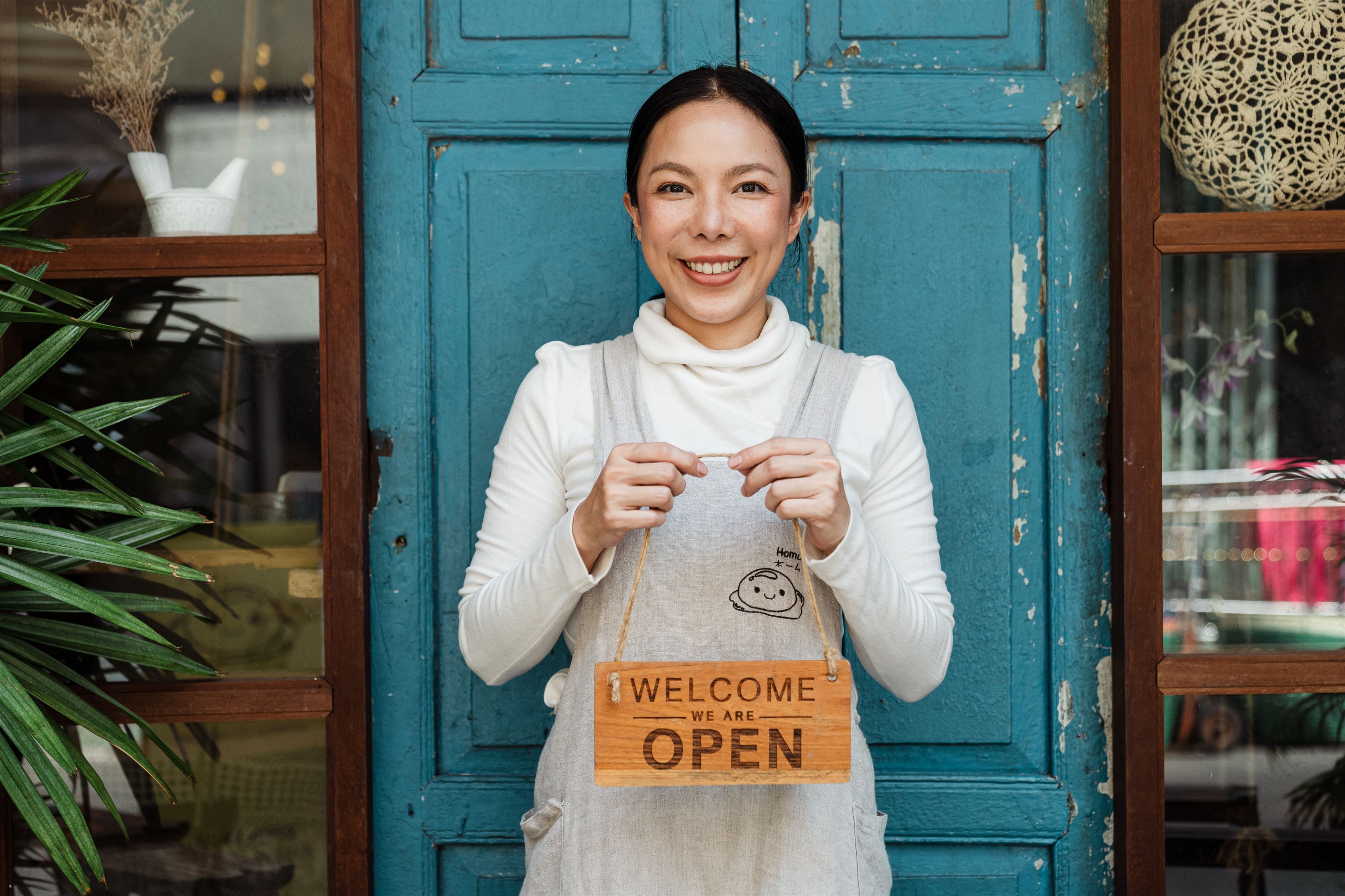 A lady business owner holding a welcome sign to her small business.